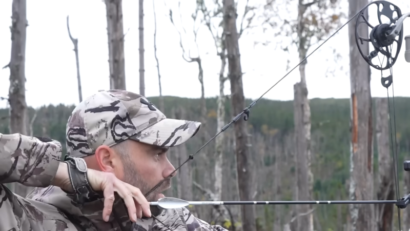 A Hunter in Camouflage Gear Aiming a Bow, Preparing to Release an Arrow in A Forested Setting