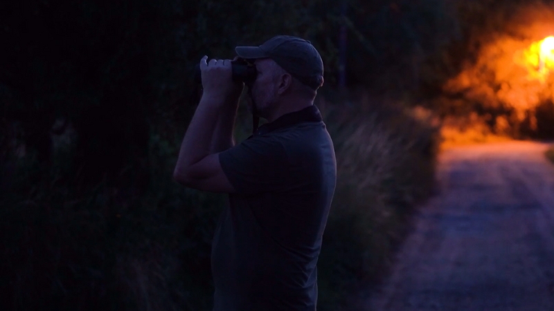 Man Using Hunting Binoculars at Dusk on A Rural Path