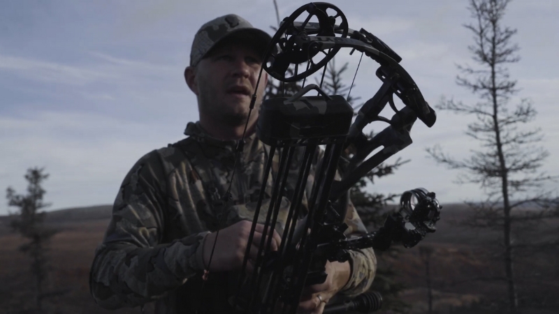 A Hunter Holding a Compound Bow in A Forested Area