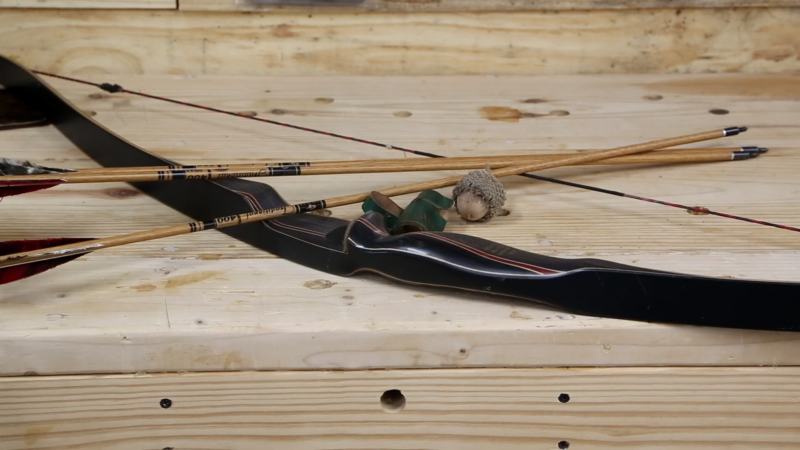 A Bear Archery Grizzly Recurve Bow with Several Arrows and Accessories on A Wooden Surface