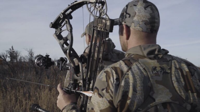 Two Hunters with Compound Bows in Camouflage Gear Walking Through Tall Grass, Choosing the Right Bow for Big Game Hunting