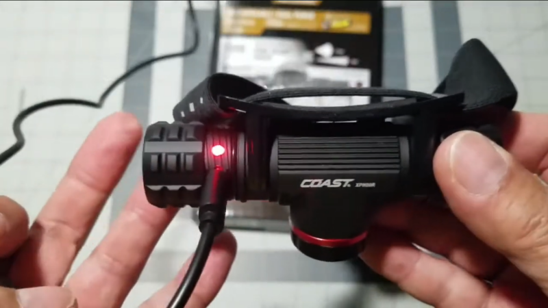 A person holds the Coast XPH30R hunting headlamp with a red light on