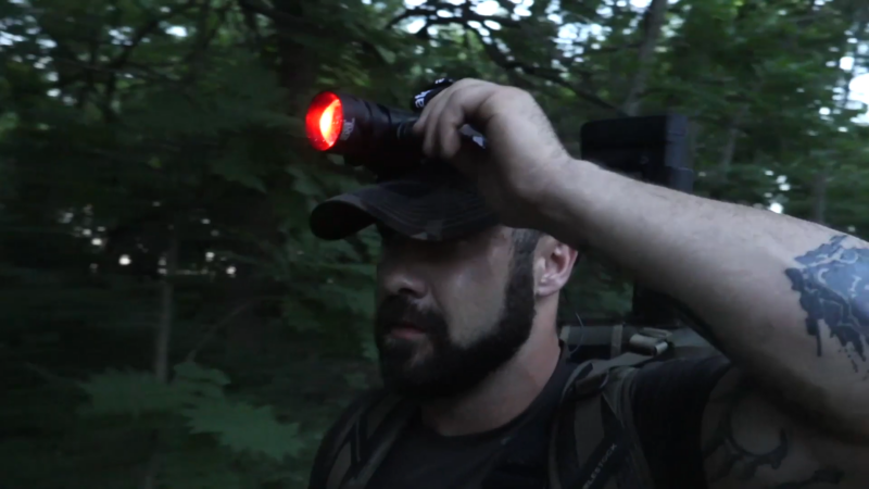 A Person Wearing a Cap Holds a Hunting Headlamp with A Red Light While Walking Through the Forest