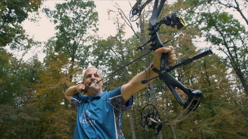 A person shooting a PSE Nock On Carbon Levitate compound bow outdoors in a forest setting