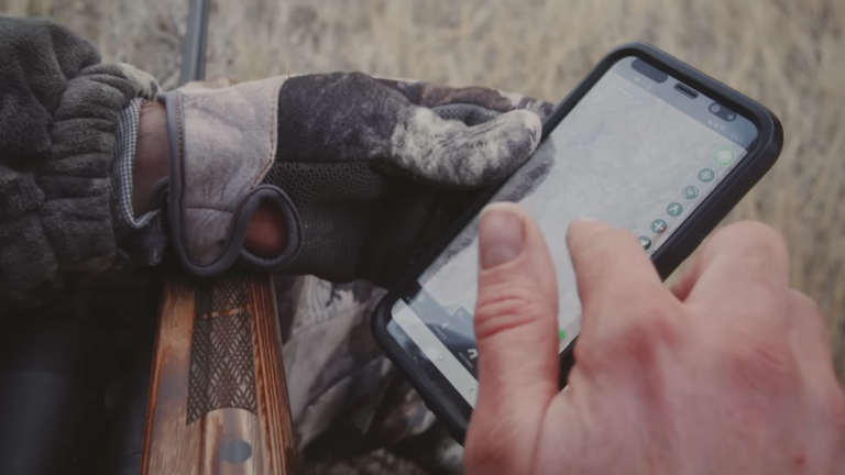 Person Using a Smartphone to Interact with A Mapping Feature of A Hunting App While Holding a Rifle